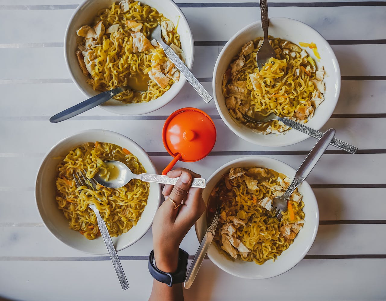 An overhead shot featuring multiple bowls of noodles with a hand reaching in, showcasing a communal meal.
